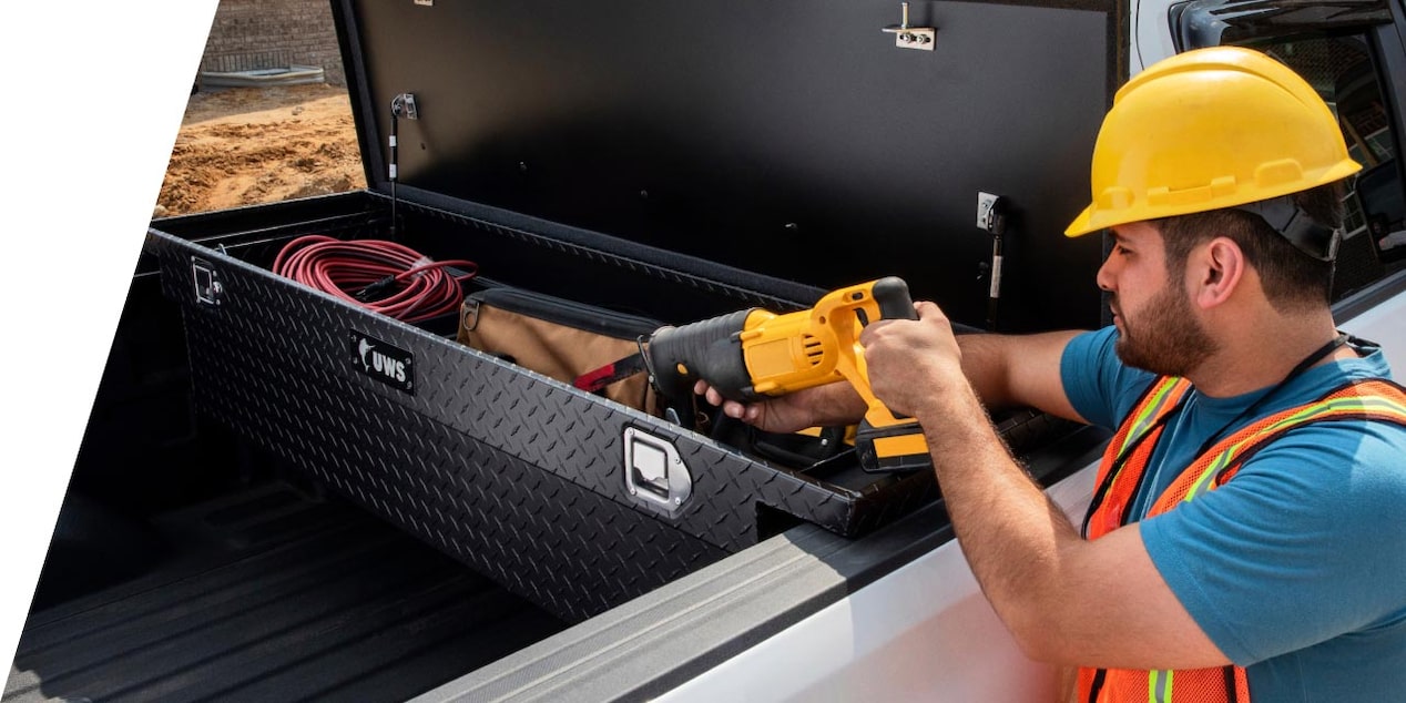A construction worker retrieving tools from their truck bed toolbox.